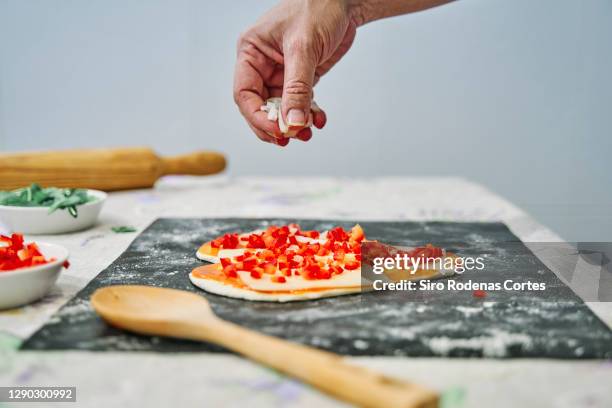 hand putting cheese on a heart shaped pizza with tomato on a table with a rolling pin and a wooden spoon - valentines day dinner stock pictures, royalty-free photos & images