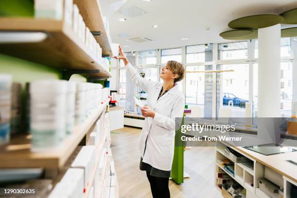 senior chemist stocking shelves in pharmacy - pharmacy imagens e fotografias de stock