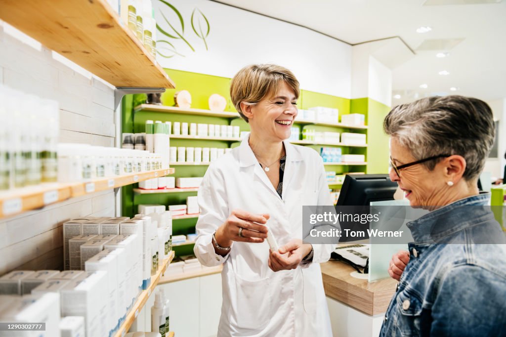 Chemist Smiling While Assisting Mature Customer In Pharmacy