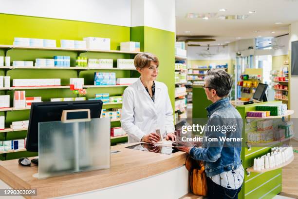 fully stocked pharmacy with chemist serving customer - apotheke stock-fotos und bilder