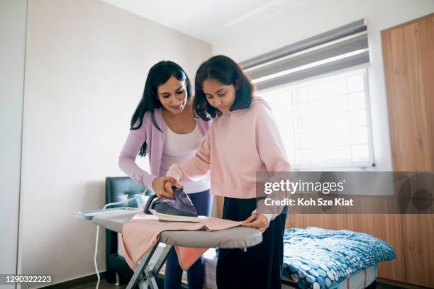 Indian mother teaches and supervises her daughter who is learning to iron laundry