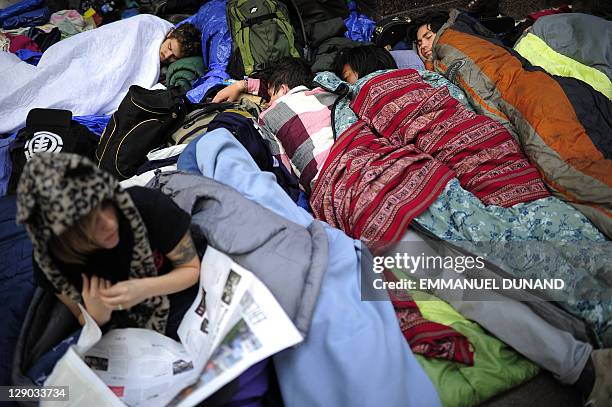 Members of Occupy Wall Street sleep while a fellow protestor reads a newspaper after spending the night on Zuccotti Park near Wall Street in New...