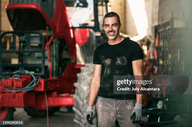 dirty worker poses next to his farm vehicle in the warehouse - agricultural-machinery-repairs stock pictures, royalty-free photos & images
