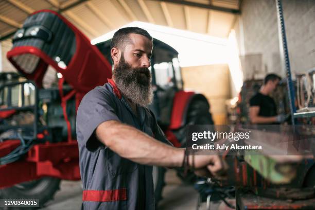 the man with the big beard mechanic of tractors with his tool adjusts parts on a lathe - agricultural-machinery-repairs stock pictures, royalty-free photos & images