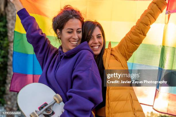 lesbian couple in the park with gay pride rainbow flag - regenbogenfahne stock-fotos und bilder