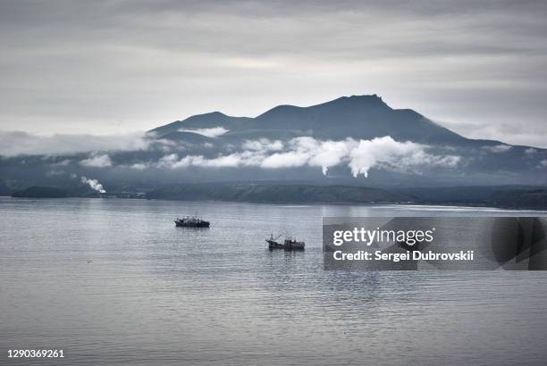 evening view on volcano of mendeleev in light fog and ships, dark gloomy sky - kuril islands stock pictures, royalty-free photos & images