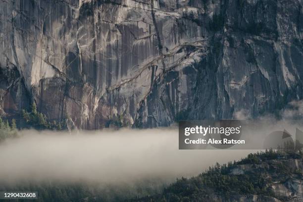 the towering rock walls of the stawamus chief with a thick layer of clouds bellow - rock face stock pictures, royalty-free photos & images