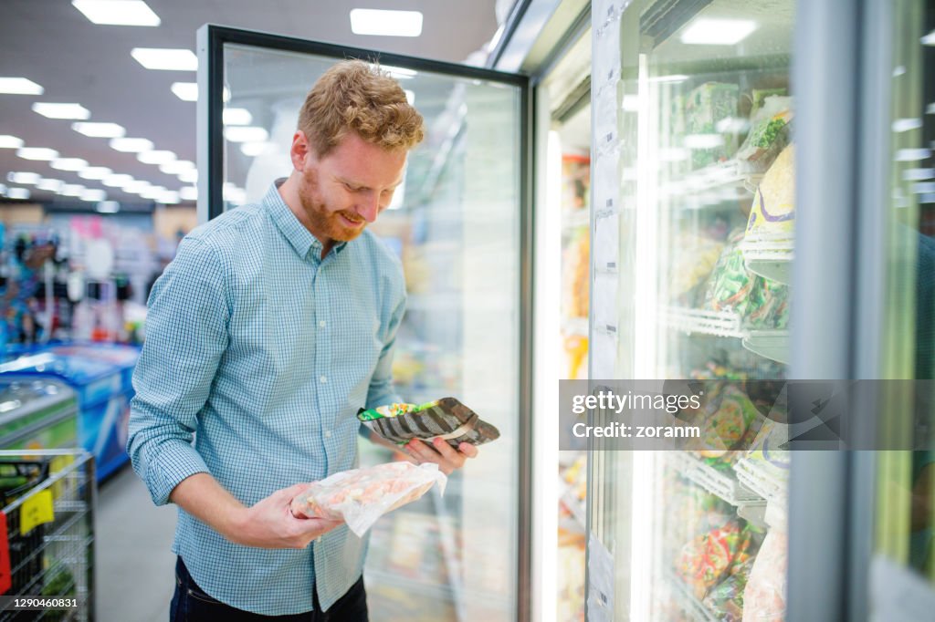 Glimlachende jonge mens die in gekoelde sectie in supermarkt kiest