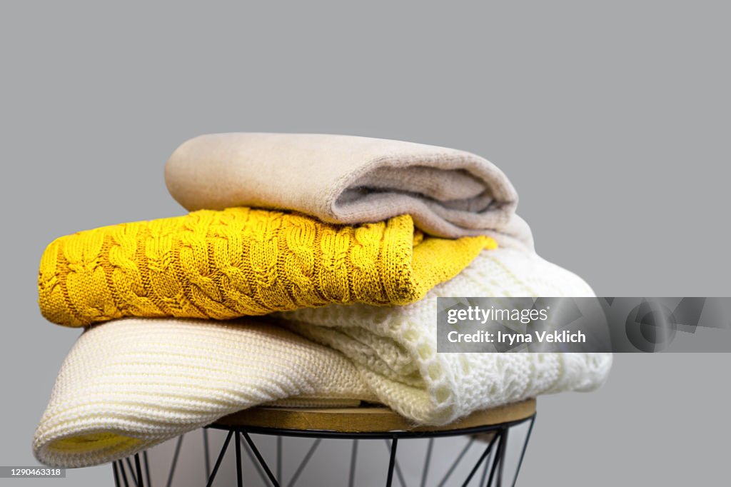 Stack of Trendy Bright illuminating Yellow, Gray and White Woolen Knitted Sweaters.