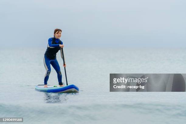 woman paddle boarding in wetsuit in sea during winter - using a paddle stock pictures, royalty-free photos & images