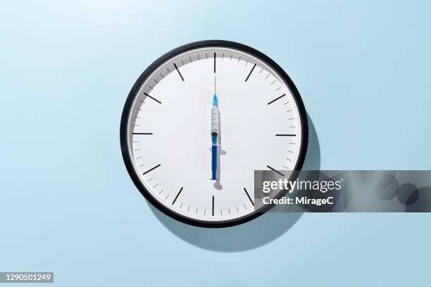 syringe as clock hand on clock face vaccination time - clocks go forward - fotografias e filmes do acervo