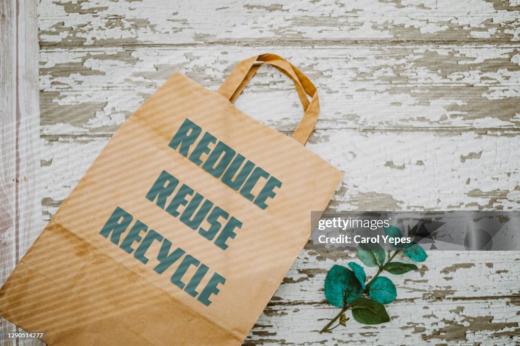 Recycled paper bag on green background. Reuse, reduce and recycle writes on it