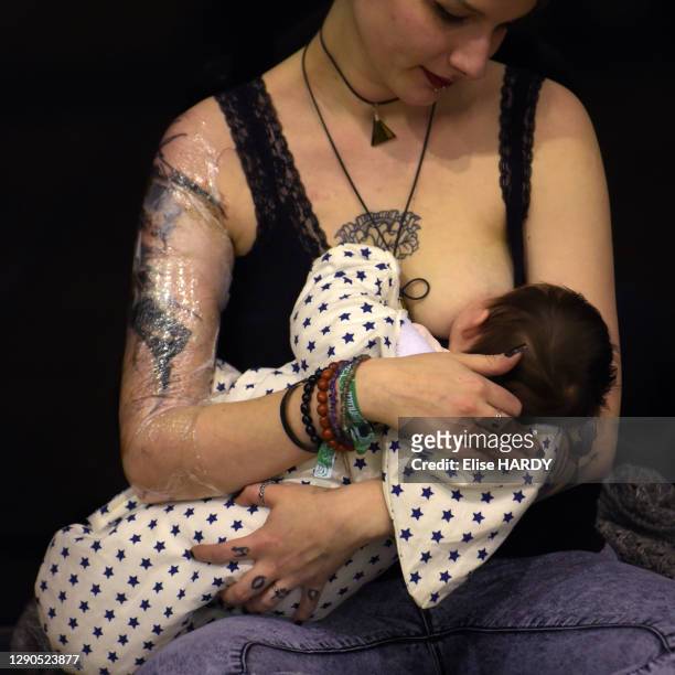 Corps tatoué d'une jeune femme allaitant son bébé au Mondial du Tatouage dans la Grande Halle de la Villette, le 5 mars 2016, Paris, France.