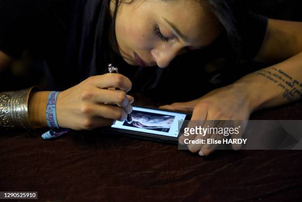 Jeune femme choisissant un dessin à tatouer sur son smartphone au Mondial du Tatouage dans la Grande Halle de la Villette, le 5 mars 2016, Paris,...