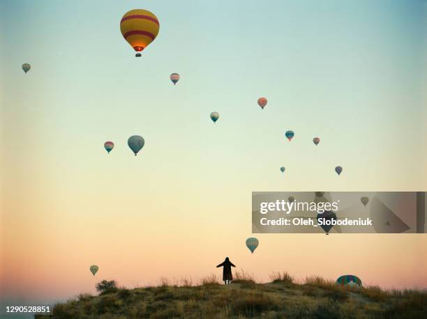 woman standing and looking at hot air balloons in  cappadocia in turkey - festival de balonismo imagens e fotografias de stock