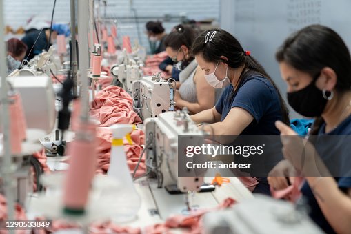 Women working at a textile factory wearing a facemask while sewing clothes Women working at a textile factory wearing a facemask while sewing clothes
