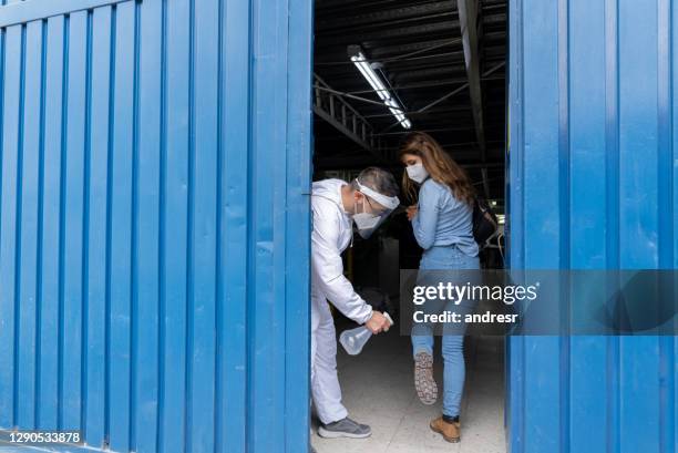 man at the door of factory applying alcohol to the shoes of the workers arriving to work - biosecurity stock pictures, royalty-free photos & images