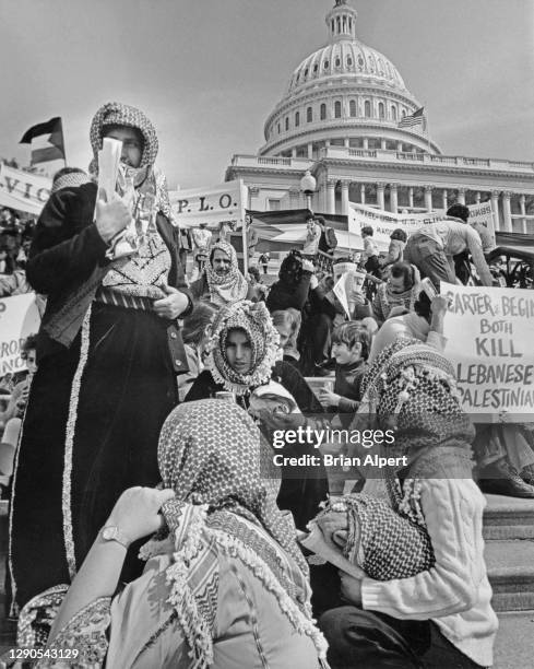 Group of protestors wearing chequered keffiyeh, with banners and placards in the background, during a pro-PLO demonstration on the steps of the...