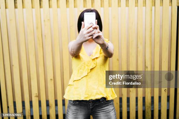 middle-aged woman with mobile phone on yellow background - obscured face phone stock pictures, royalty-free photos & images