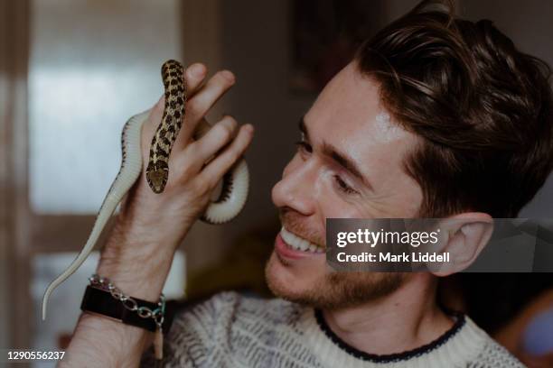 young man holding a pet garter snake indoors - garter snake fotografías e imágenes de stock