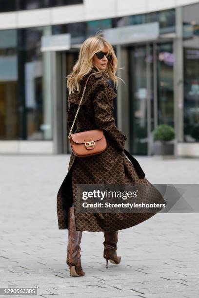 Influencer Gitta Banko wearing a dark brown trenchcoat with 70's triomphe print by Celine, a cognac colored chain bag with gold triomphe details by...