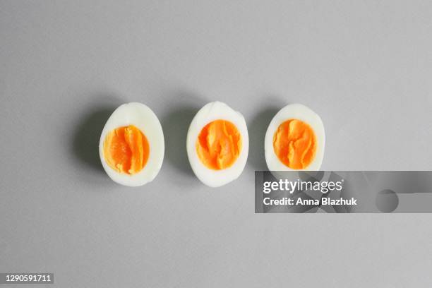 boiled eggs in row with yellow yolk over gray background. trendy pantone's colors of 2021 year, ultimate gray and illuminating yellow, abstract background - gekochtes ei stock-fotos und bilder