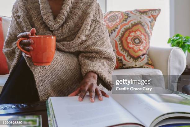 woman reads book in living room - coffee table books stockfoto's en -beelden