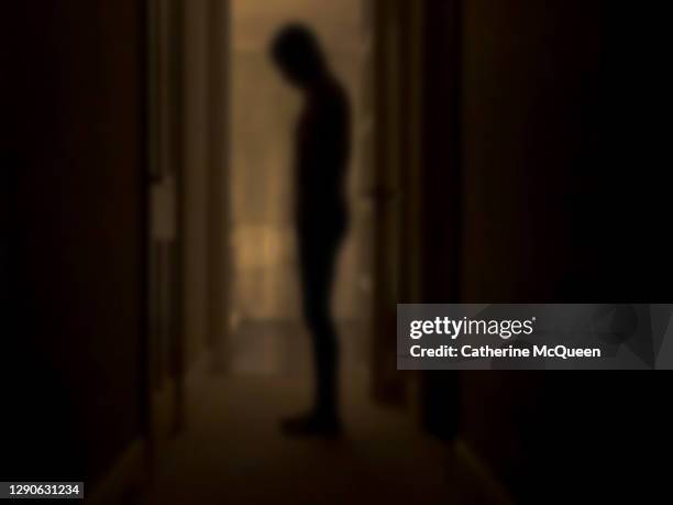 silhouette of depressed person standing in dark room - winterdepression stock-fotos und bilder