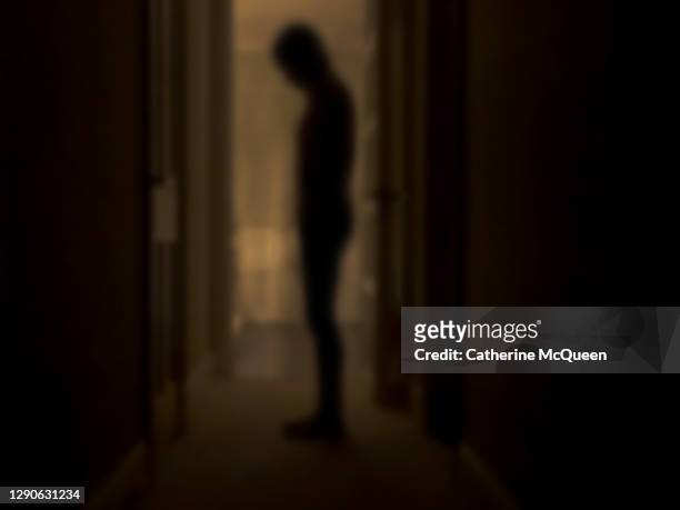 silhouette of depressed person standing in dark room - locura fotografías e imágenes de stock