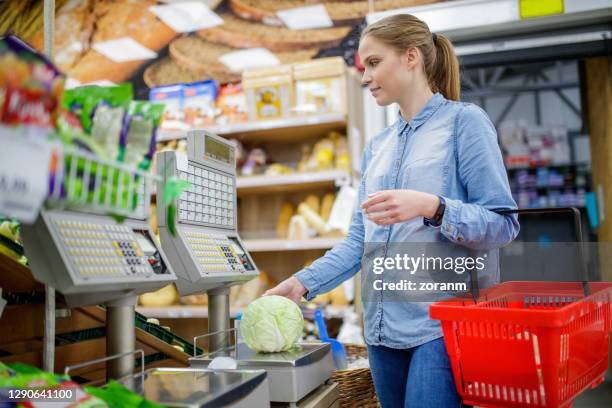 young woman measuring cabbage on scale in supermarket - self service stock pictures, royalty-free photos & images