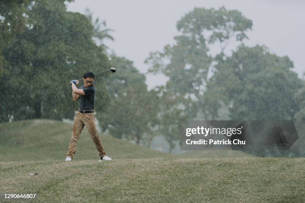 mature asian chinese man golfer ready to teeing off in the rain at golf course - bad golf swing stock pictures, royalty-free photos & images