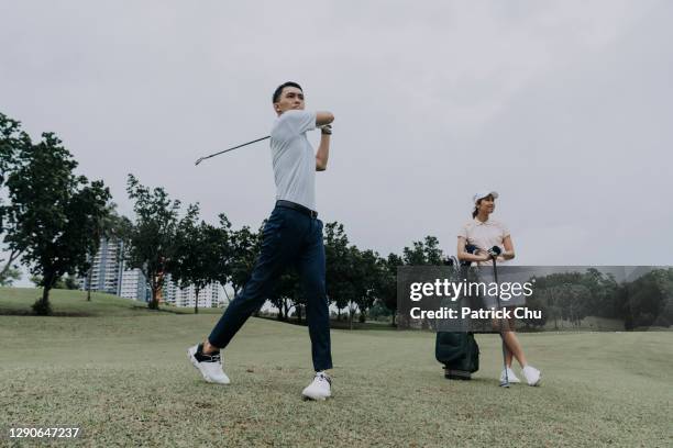 asian chinese mature man golfer swinging his golf club while his friend is observing at golf course - country club stock pictures, royalty-free photos & images