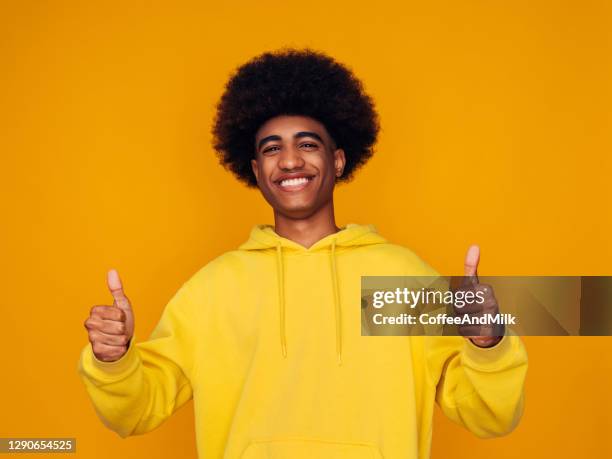 smiling young guy wearing yellow hoodie and showing thumbs up - hoodie stock pictures, royalty-free photos & images