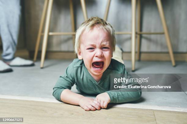 a little boy with blond hair, two years old, is lying on the floor and crying hysterically after kindergarten at home. parenting. - toddler photos et images de collection