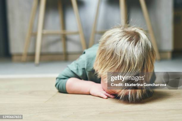 a little boy with blond hair, two years old, is lying on the floor and crying hysterically after kindergarten at home. parenting. - trotzanfall stock-fotos und bilder