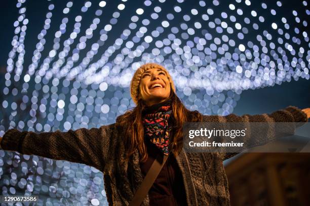 young smiling woman standing on well decorated town square with christmas lights and spinning - luzes de natal imagens e fotografias de stock
