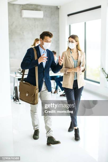 business colleagues walking through the modern office with covid19 masks on their faces - employee engagement mask stock pictures, royalty-free photos & images