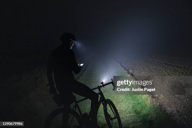 cyclist checking for directions on smartphone whilst out in the countryside on a dark foggy evening - fahrradlampe stock-fotos und bilder