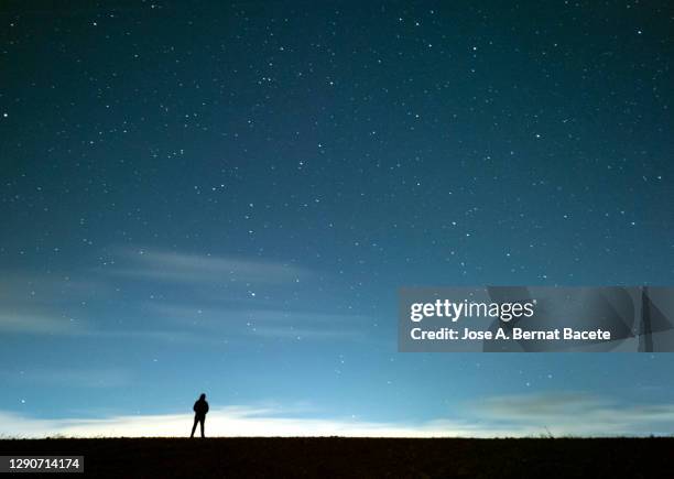 silhouette of a person lost in the field at night with a blue sky full of stars. - moody sky stockfoto's en -beelden
