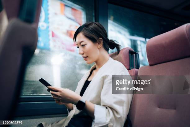 young asian woman using smartphone while commuting by public transportation in a bus after work in the city at night, with illuminated commercial signs in background - angeleuchtet zahlen mensch stock-fotos und bilder