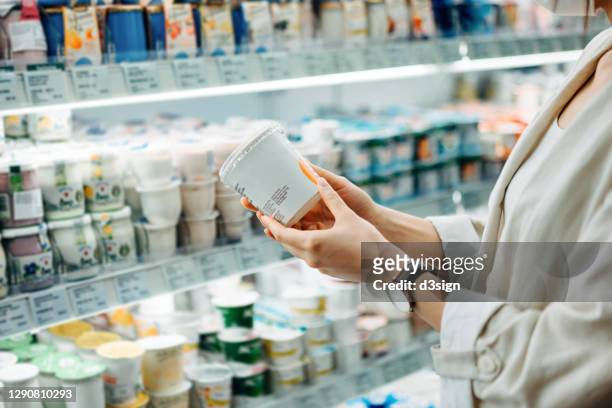 cropped shot of young asian woman shopping in the dairy section of a supermarket. she is reading the nutrition label on a container of fresh organic healthy natural yoghurt - supermarket fridge stock pictures, royalty-free photos & images