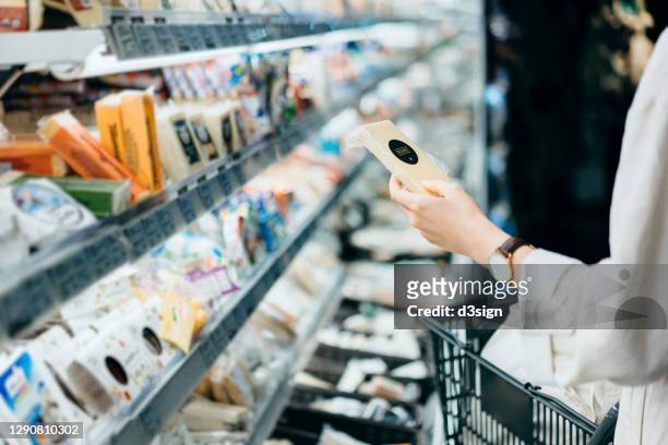 cropped shot of young asian woman with a shopping cart, shopping in the dairy section of a supermarket. she is reading the nutrition label on the package of a fresh organic cheese - cheese stock pictures, royalty-free photos & images