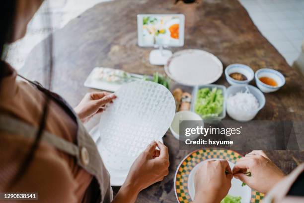 two young asian women making vietnamese spring rolls and using digital tablet for online tutorials - goi cuon stock pictures, royalty-free photos & images