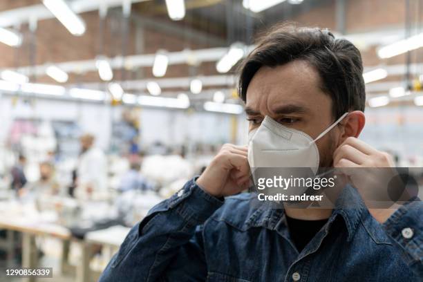 hombre trabajando en la fábrica textil durante la pandemia covid-19 y arreglando su mascarilla - mascarilla n95 fotografías e imágenes de stock