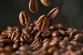 Close up of roasted coffee beans on a black smokey background.