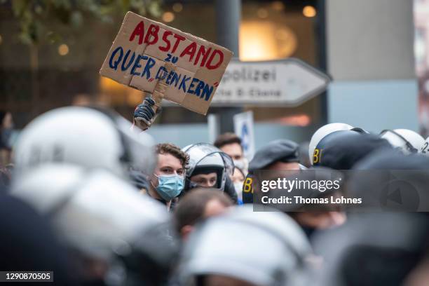 Young counter-demonstrator with a sign 'Abstand zu Querdenkern' stands near police officers and opponents of what they claim are restrictions to...