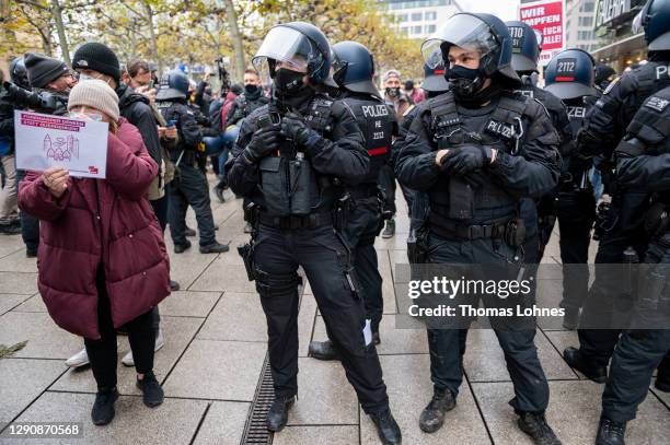 Counter-demonstrator stands next to police officers in front of opponents of what they claim are restrictions to their personal freedoms due to...