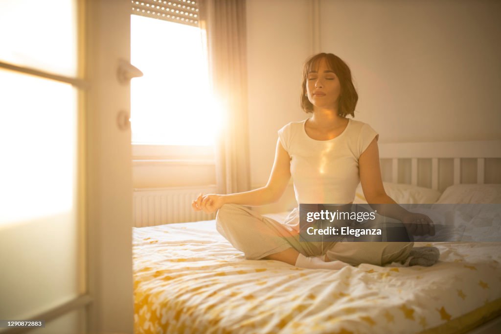 Beautiful woman waking up in her bed, she practicing yoga. Young beautiful woman waking up in her bed fully rested. Woman exercising yoga in bed after wake up.