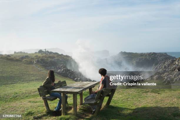 boy and girl sitting an outdoor table near the sea, connection with nature - llanes stock-fotos und bilder