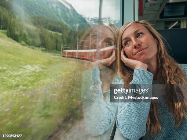 woman traveling by train looking from the window enjoying passing scenery - switzerland train stock pictures, royalty-free photos & images